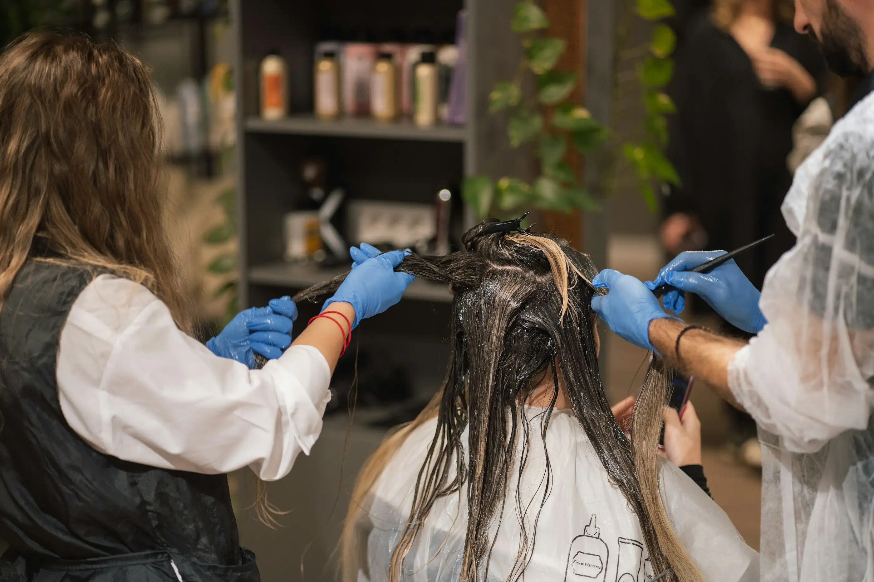 Two colourists in gloves painting colour through a client's hair in a salon