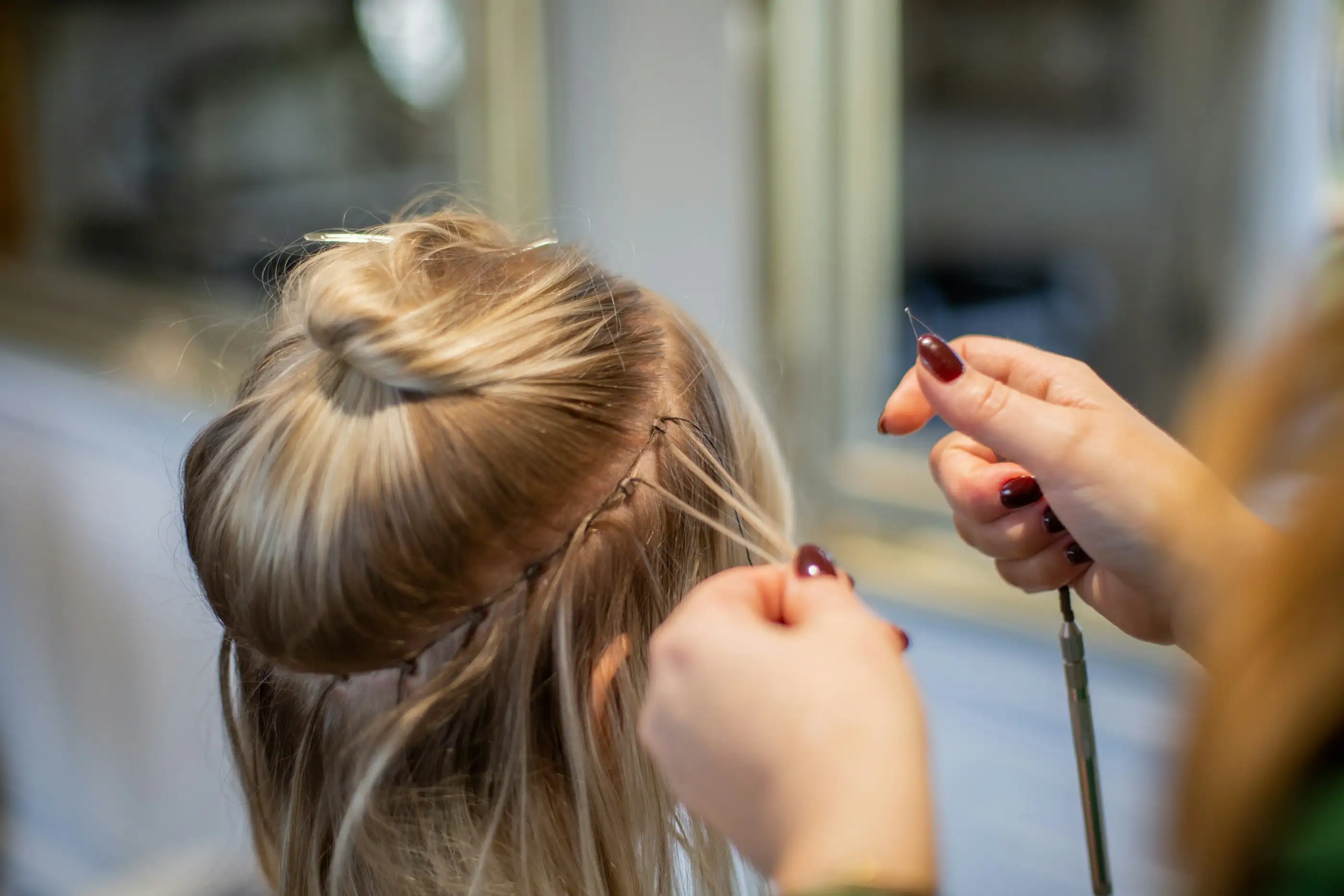 A stylist's hands fitting extensions into blonde hair pinned up in a bun