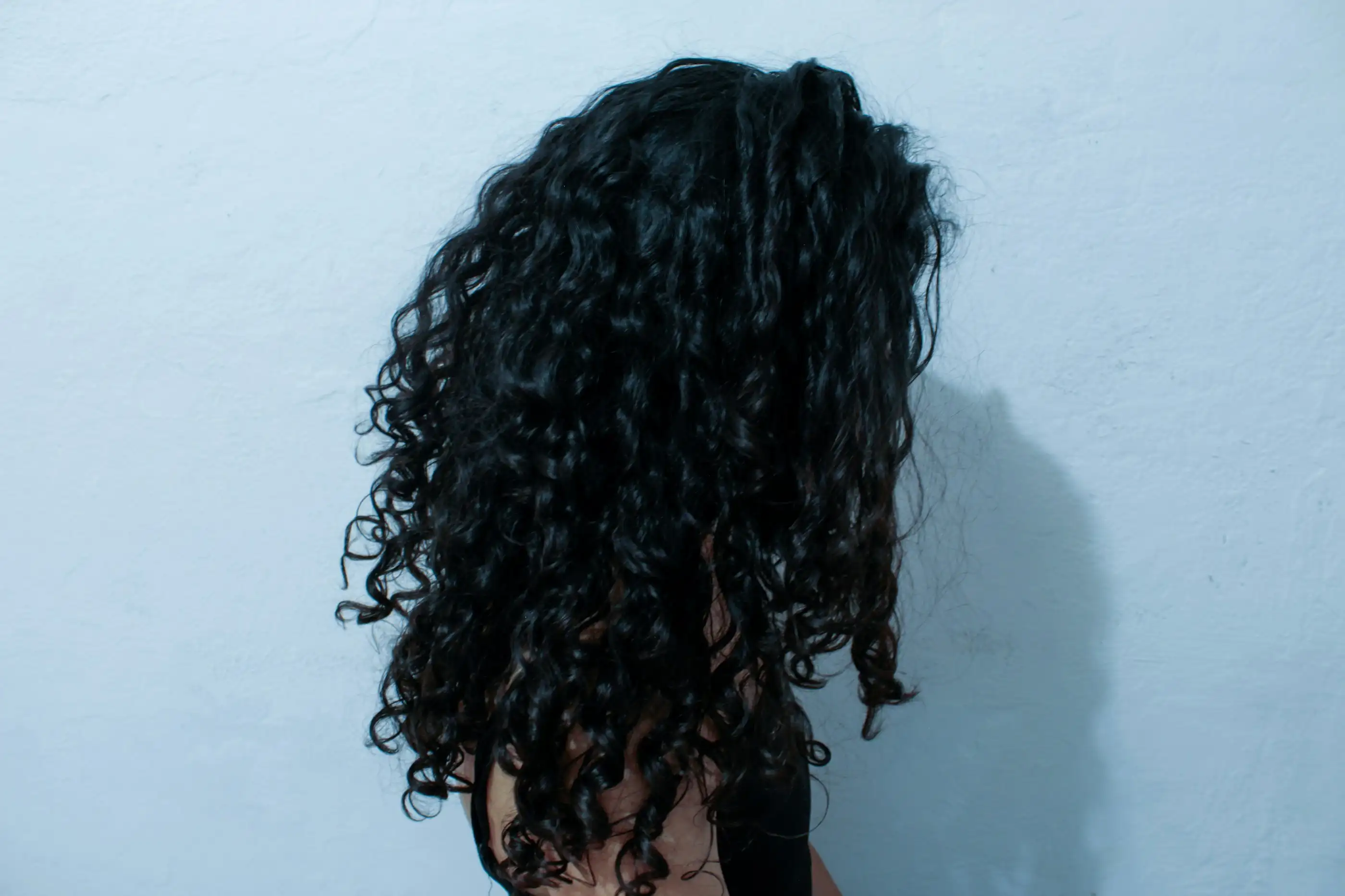 Thick, tight black curls seen from behind against a pale blue wall