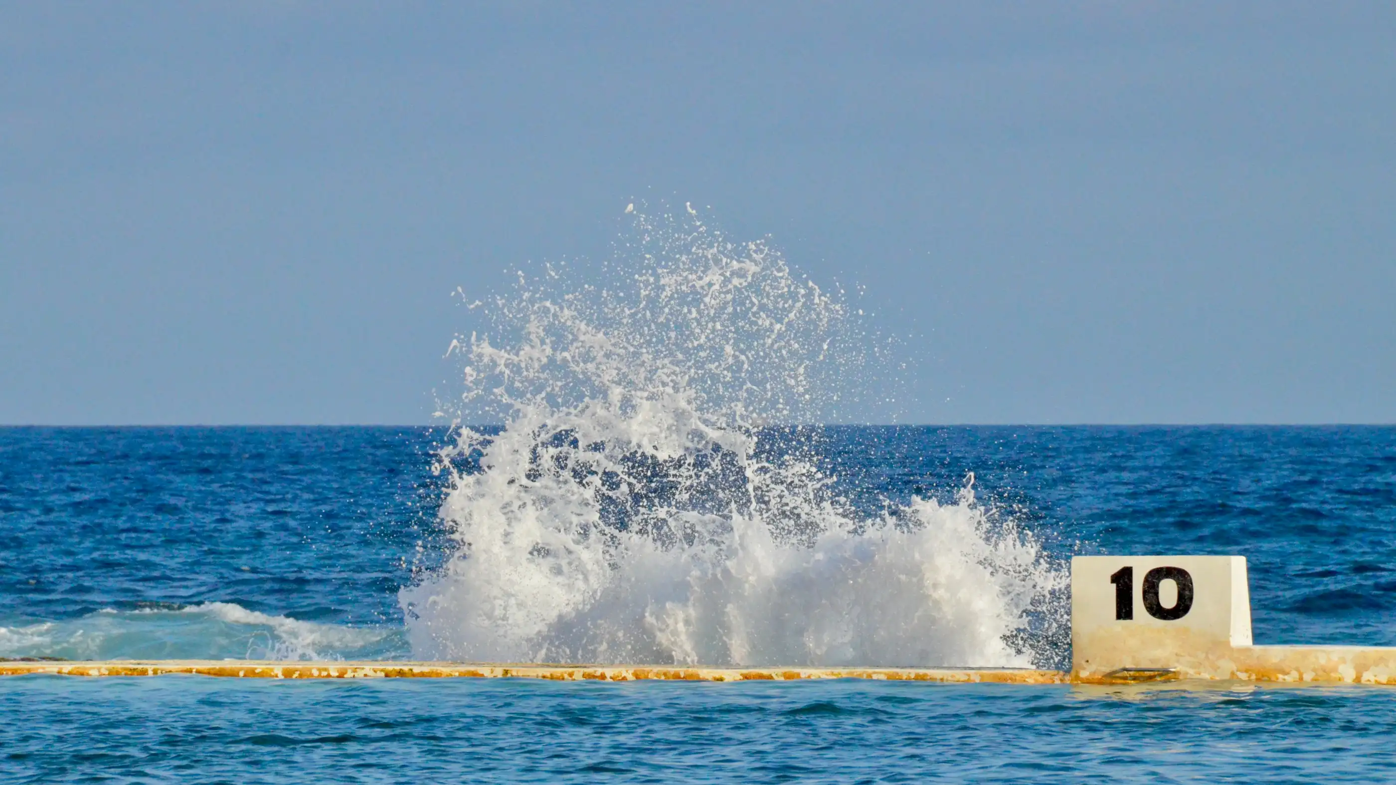 A wave breaking over the edge of Merewether Ocean Baths beside the lane 10 marker