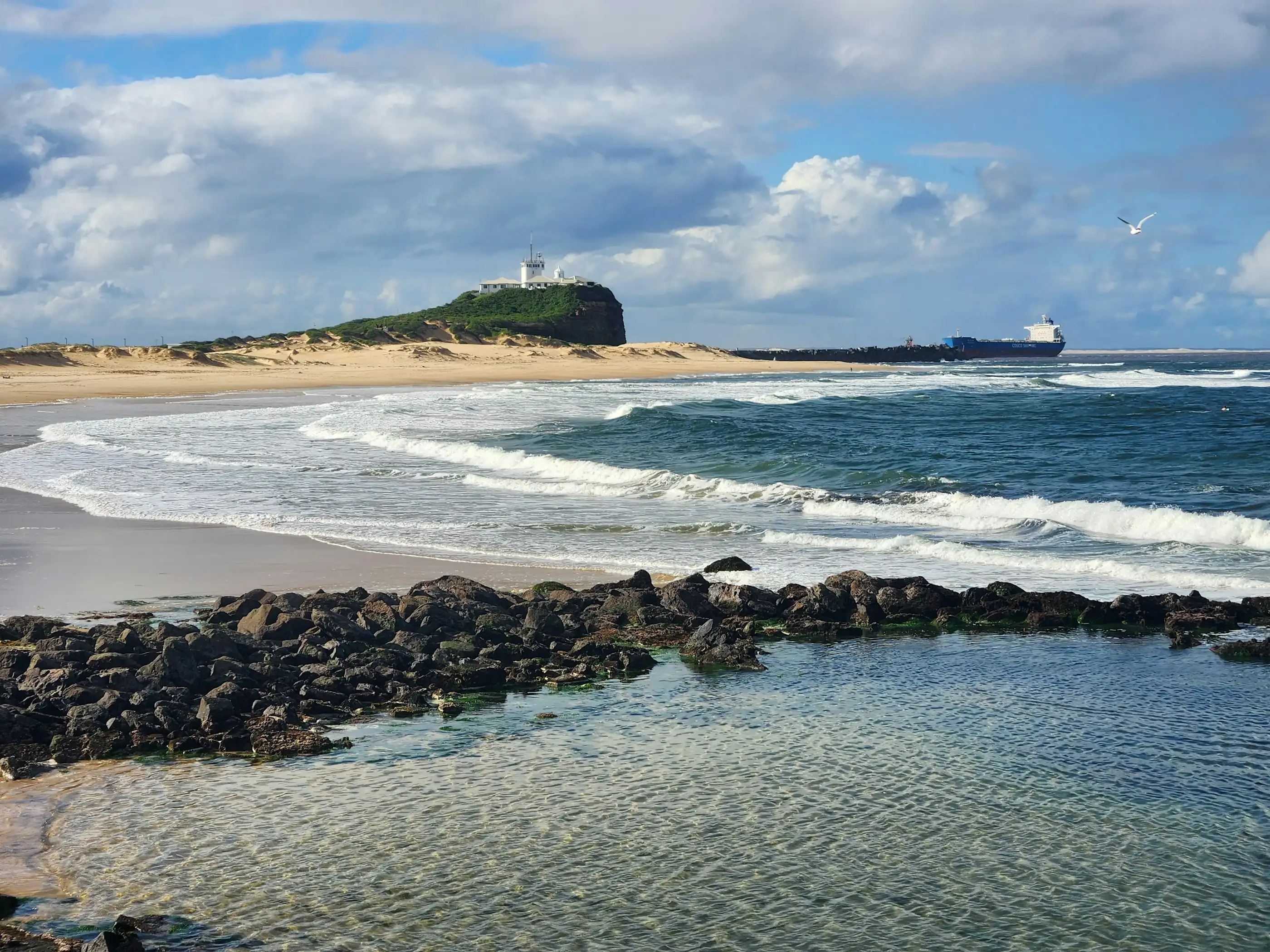 Nobbys Beach and the Nobbys Head lighthouse, with a ship on the horizon