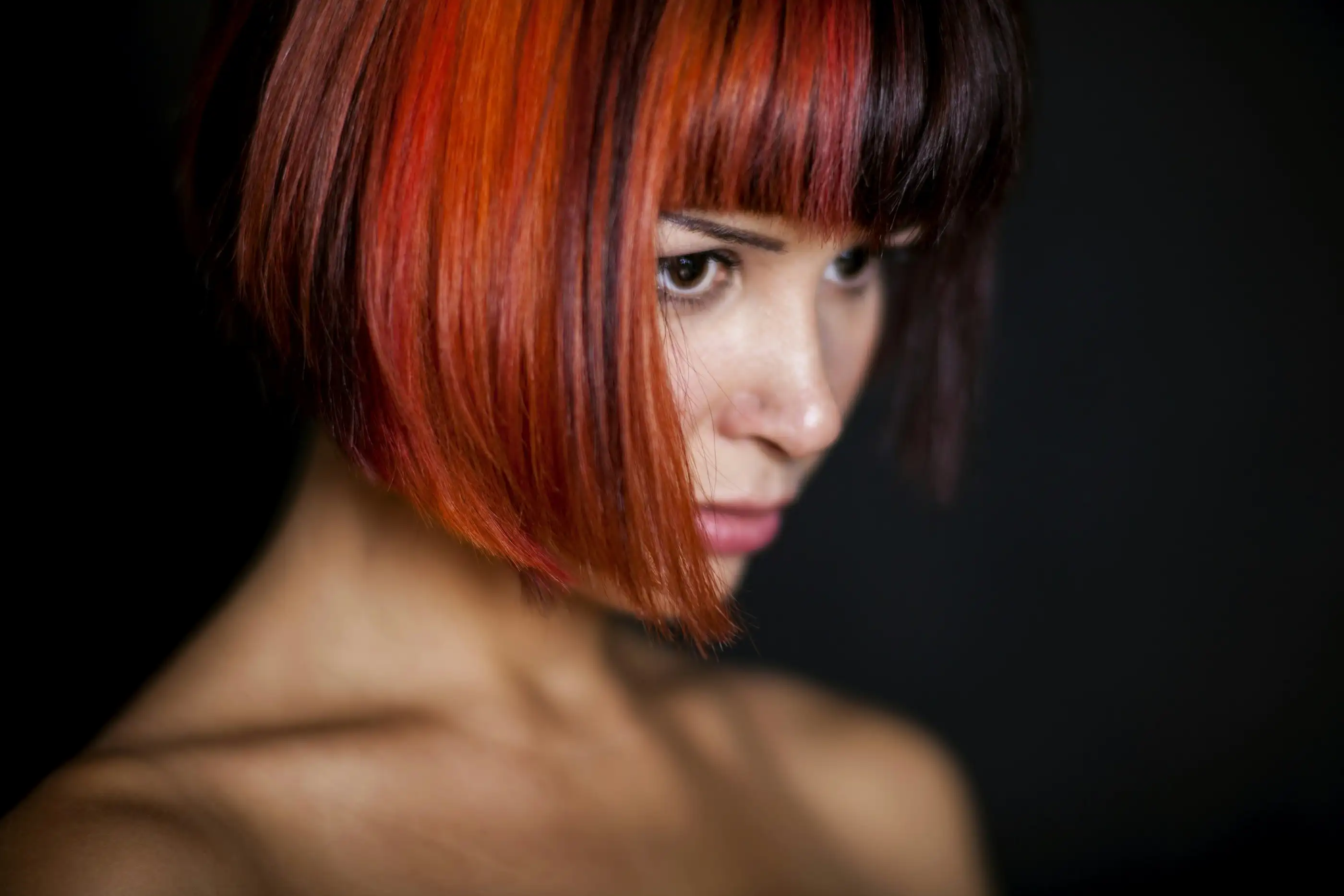 A woman with a sharp, glossy bob and a heavy fringe, looking down to one side