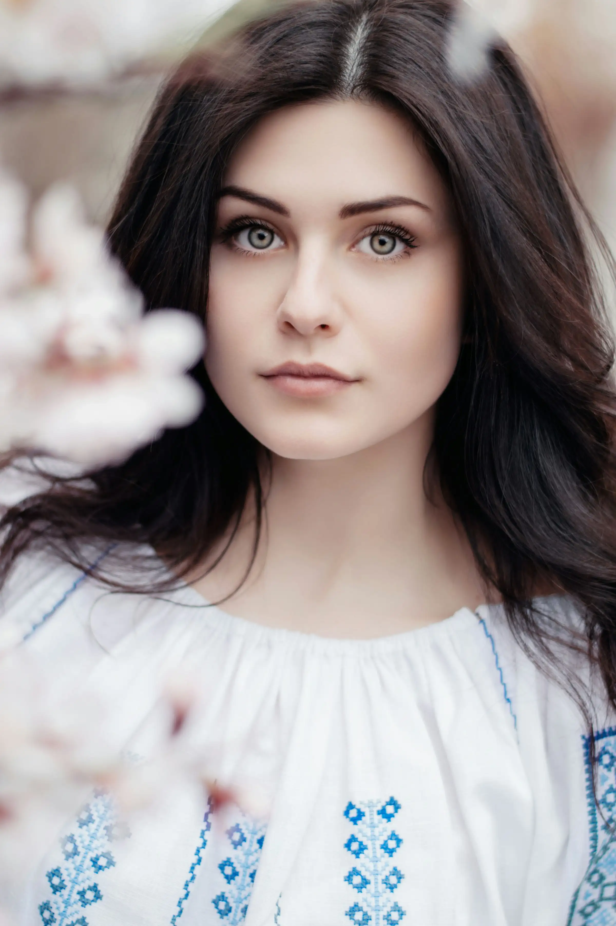 A woman with long dark hair and pale eyes, framed by white blossom