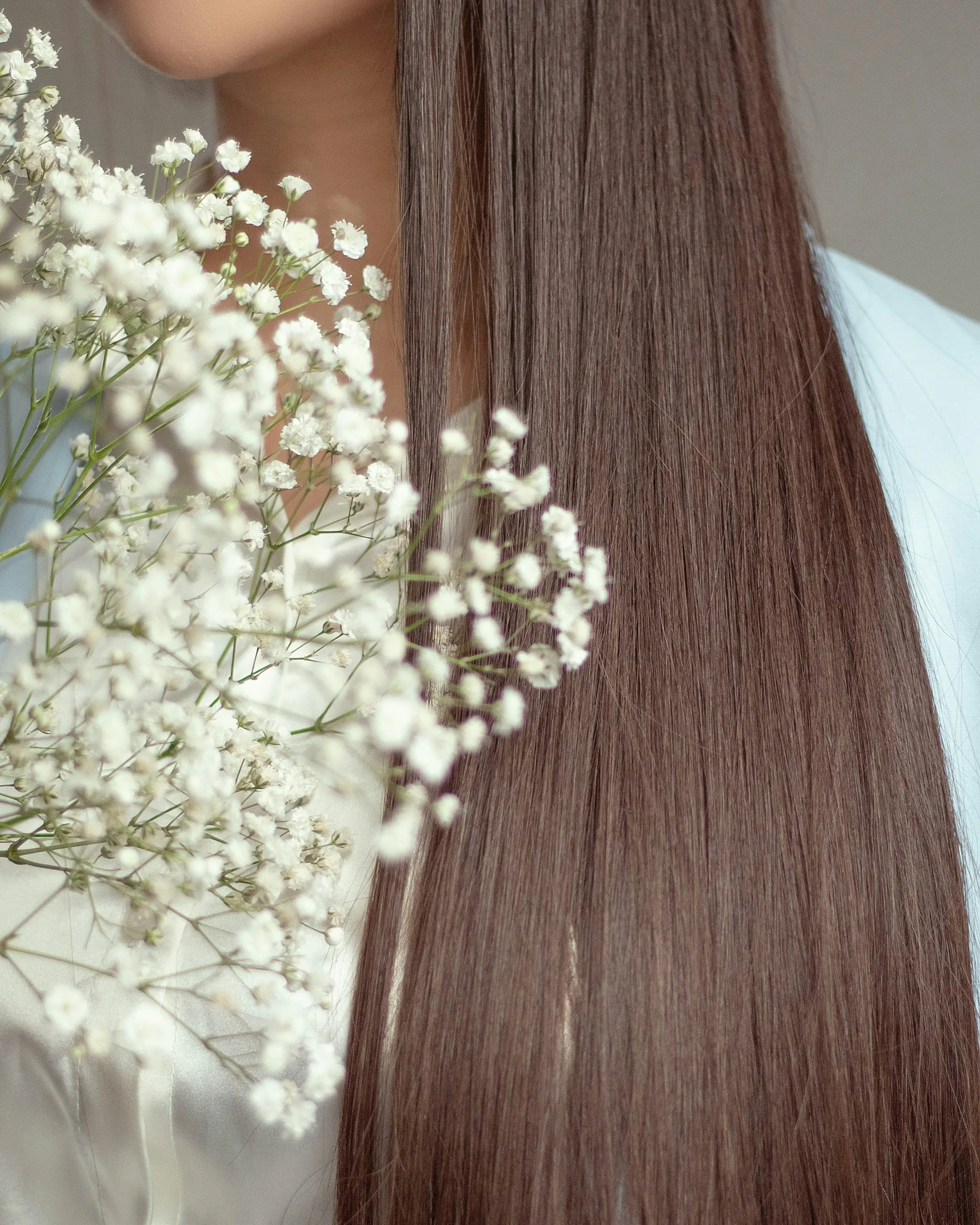 Long, sleek, straight brunette hair beside a spray of white gypsophila